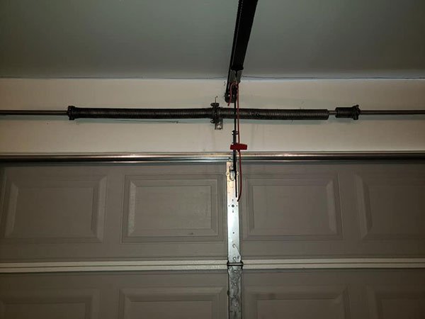A faulty garage door mechanism, close-up on the springs, the hockey stick, and opener carriage