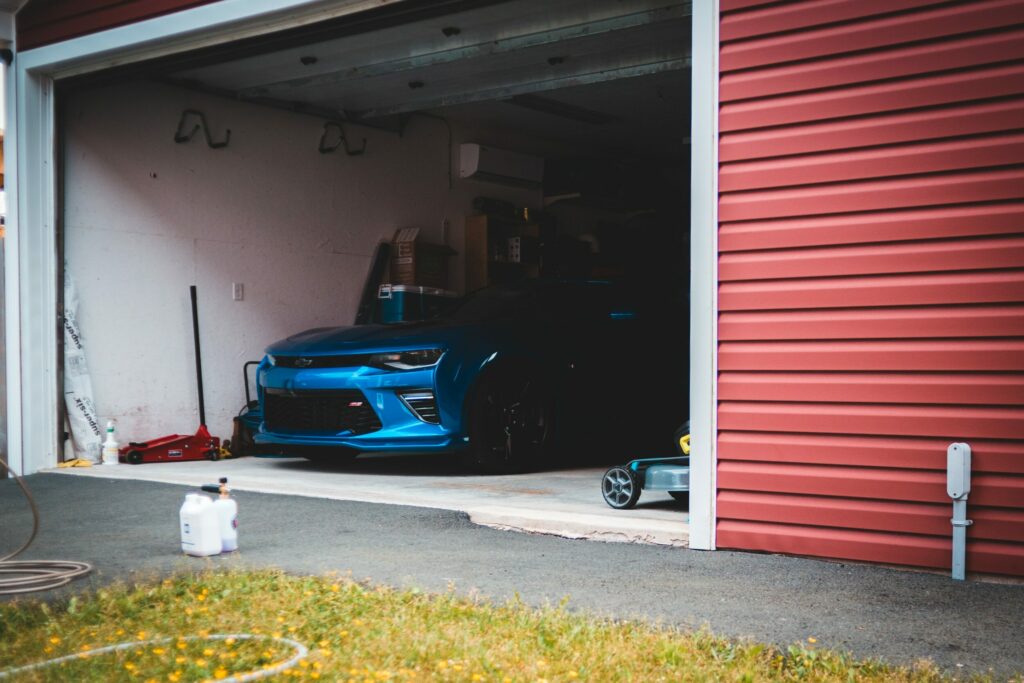 an image showing a blue sedan parked inside an open garage door with broken spring.
