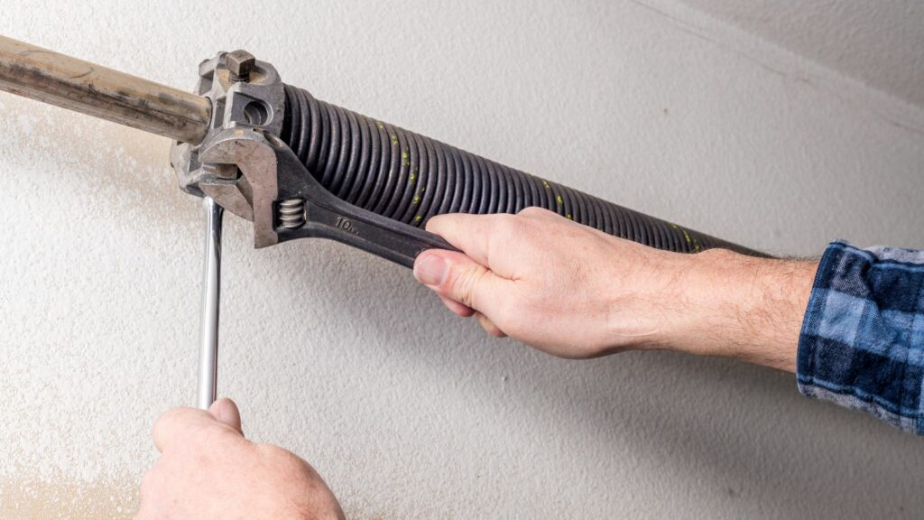 A professional fixing a garage door using its wrench.